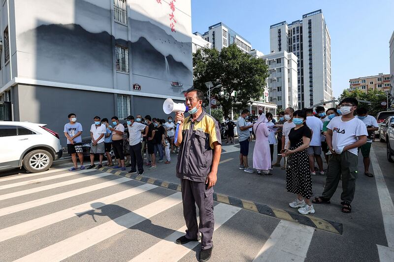 2021年7月31日,一名男子在郑州通过扬声器维持秩序,居民排队接受新冠核酸检测。